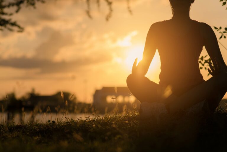 Young woman peacefully meditating in a open field. Happy young woman sitting outdoors in yoga position. Young girl practicing yoga outdoors.